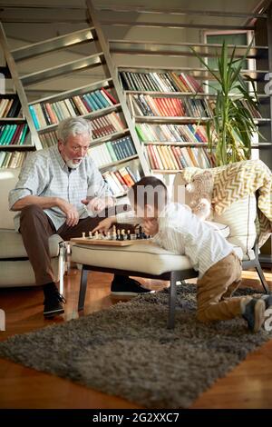 Opa ist begeistert, als er mit seinem kleinen Enkel in einer verspielten Atmosphäre zu Hause das Schach spielt. Familie, Spiel, zusammen Stockfoto