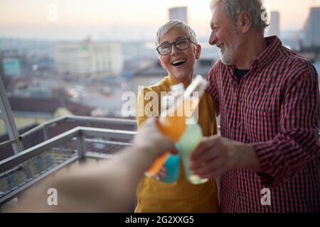 Ein älteres Paar, das eine gute Zeit hat, während es einen Drink mit etwas Gesellschaft in einer fröhlichen Atmosphäre auf der Terrasse einer Wohnung in einem schönen s genießt Stockfoto