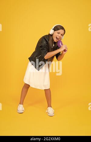 Imaginäre Bühne. Singen Sie wie ein Rockstar. Haarbürstenmikrofon. Musik hören. Mädchen mit Kopfhörern. Hobby-Konzept. Glückliches Kind in Kopfhörern. Audiokonzept Stockfoto