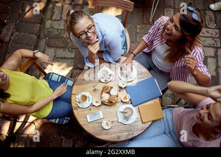 Draufsicht auf kaukasische Freundinnen, die im Café im Freien am Tisch sitzen, Kaffee trinken, lachen, reden Stockfoto