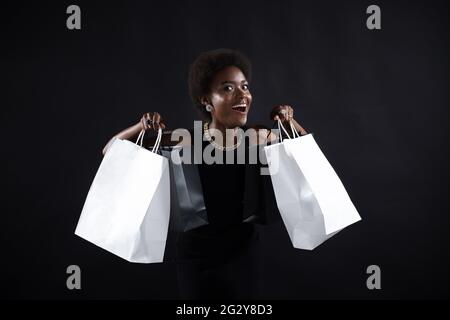 afroamerikanische verblüffte Frau mit Afro-Frisur hält schwarze und weiße Einkaufstaschen. Verkauf und Rabatte auf Markt und Black Friday Konzept. Stockfoto