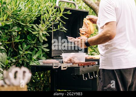 Mann beim Grillen von Fleisch auf einem Grill verschiedene Fleischsorten, Huhn, Würstchen, Blutwurst, Lamm auf einem Crbon-Grill im Garten Stockfoto