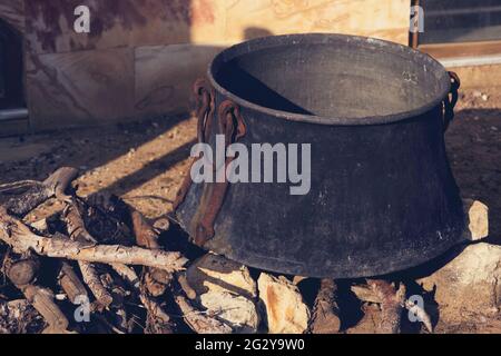 Kochen in rußigem alten Kessel am Lagerfeuer an sonnigen Tagen. Nahaufnahme. Retro getöntes Bild. Stockfoto