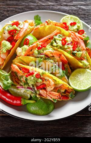 Nahaufnahme von Taco-Muscheln mit gegrillten Garnelen, Kohlsalat, Limette und Guacamole auf einem Teller auf einem Holztisch Stockfoto