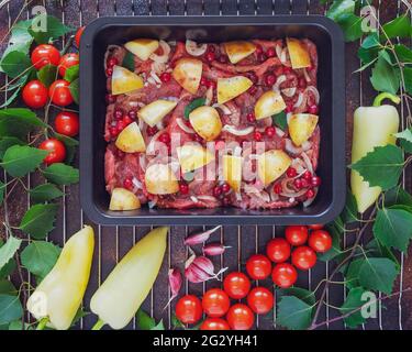 Kochen von Fleisch mit Bauerngemüse unter freiem Himmel. Lebensmittelzusammensetzung mit einem Backblech mit Rindfleisch, neuen Kartoffeln und Beeren auf einem Grill mit Birkenzweigen Stockfoto