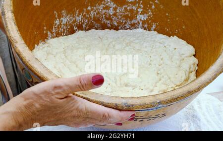 Eine Frau hält eine große, authentische Tonschüssel mit Hefeteig aus der Nähe. Kochen zu Hause. Meisterklasse über die Herstellung von süßen Donuts. Stockfoto