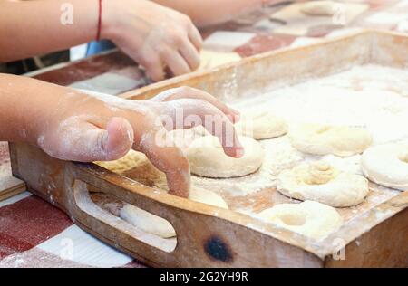 Das Kind macht mit dem Finger ein Loch für den Donut. Kochen zu Hause. Meisterklasse über die Herstellung von süßen Donuts. Stockfoto