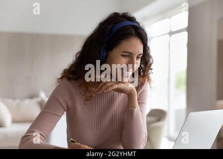 Lächelnde Latino-Frau in Kopfhörern arbeitet auf einem Laptop Stockfoto