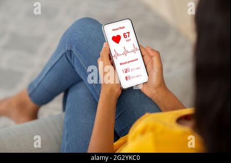Schwarze Dame chillt zu Hause, mit Gesundheit App auf dem Smartphone Stockfoto