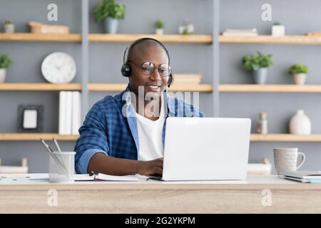 Hotline-Support-Service. afroamerikanischer, männlicher Callcenter-Mitarbeiter im Headset, der zu Hause mit einem Laptop arbeitet Stockfoto