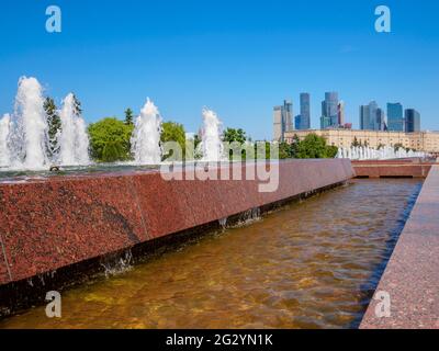 Jets von Springbrunnen an einem sonnigen Tag vor der Kulisse moderner Wolkenkratzer und einem wolkenlosen blauen Himmel. Erholungsgebiet im Victory Park auf Poklonnaya Stockfoto