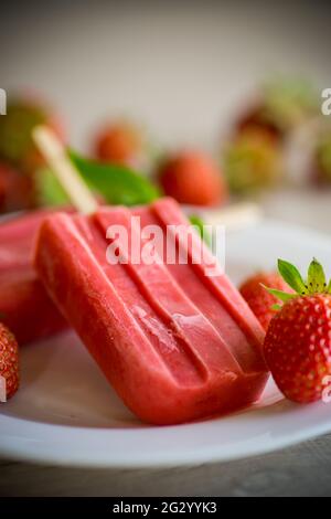 Hausgemachtes Erdbeereis auf einem Stock aus frischen Erdbeeren auf einem Teller auf einem Holztisch Stockfoto