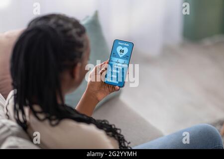 Junge schwarze Dame, die ihre Herzfrequenz auf dem Handy überprüft Stockfoto