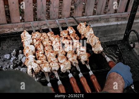 Der Koch bereitet Chicken Shish Kebab zu. Turkish Street Food. Fleisch über einem Feuer gekocht, Grillparty im Hinterhof. Männliche Hände in Handschuhen halten Stahlspieß Stockfoto