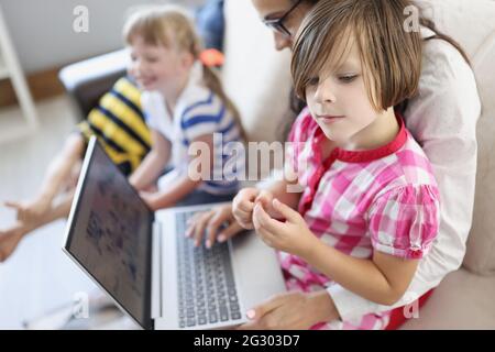 Frau arbeitet auf ihrem Schoß aus der Ferne auf dem Laptop, und Kinder spielen in der Nähe Stockfoto
