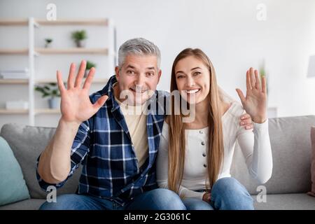 Positives reifes Paar, das einen Videoanruf abgibt, vor der Webcam winkt und modernes Gadget für die Fernkommunikation zu Hause verwendet Stockfoto