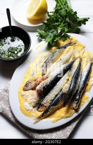 Sardinenfisch. Gesunde Ernährung. Fisch gereinigt und in Mehl eingeweicht. Auf einem hölzernen Kiebel mit Zitrone, frischer Petersilie, Schüssel mit Sauce der Petersilie. Direkt darüber. Stockfoto