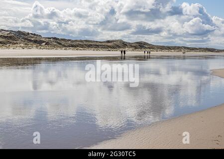 Strand, Wasser, das weiße Wolken reflektiert, Menschen, die mit Dünen im Hintergrund wandern, bewölktes Wetter mit reichlich Wolken am Himmel in Hargen aan Zee, Norden Stockfoto