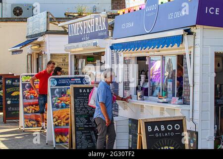 Die Menschen stehen Schlange, gesellschaftlich distanziert, für Eis und Fish & Chips, an Imbissständen am Strand von Lyme Regis, Jurassic Coast, Dorset, England Stockfoto
