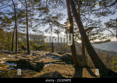 Winterlandschaft im Wald mit Paar, das bei Sonnenuntergang im goldenen Licht auf der Bank sitzt, Mullerthal, Luxemburg Stockfoto