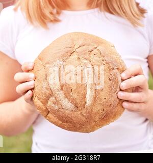 Das Kind hält ein rundes Brot. Gesunde Ernährung. Großes frisches Bäckerbrötchen tragen Stockfoto