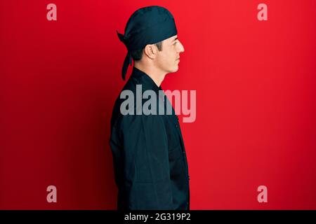 Hübscher junger Mann in professioneller Koch-Uniform und einem Hut, der zur Seite schaut, relax Profil Pose mit natürlichem Gesicht mit selbstbewusem Lächeln. Stockfoto