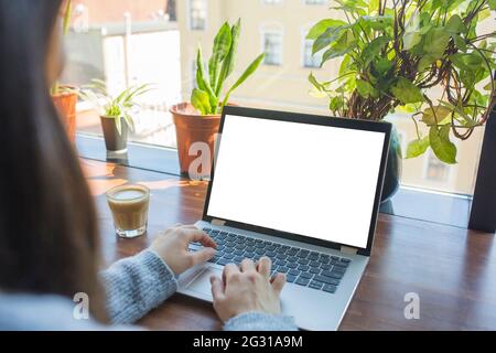 Nachbildung einer Frau, die einen Laptop mit leerem weißen Desktop-Bildschirm beim Kaffeetrinken verwendet. Stockfoto