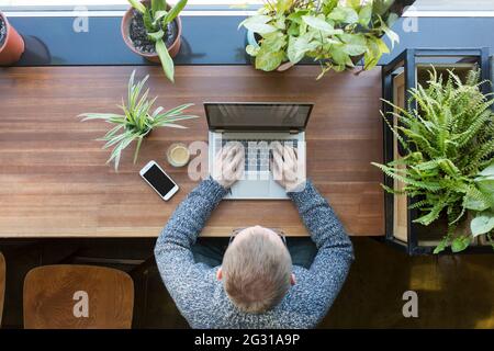 Ein vielbeschäftigter Geschäftsmann, der mit einem Laptop am Holzschreibtisch arbeitet. Stockfoto