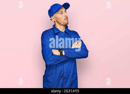 Glatze Mann mit Bart trägt Baumeister Jumpsuit Uniform Blick zur Seite mit gekreuzten Armen überzeugt und zuversichtlich Stockfoto