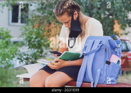 Schulmädchen auf der Straße mit einem Lehrbuch und in einer Schutzmaske. Stockfoto