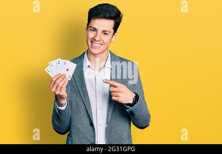 Junger hispanischer Geschäftsmann spielt Poker und hält Karten, die lächelnd mit Hand und Finger zeigen Stockfoto