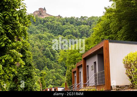 Burg Bourscheid am Fluss Sûre. Im Vordergrund Bungalows des Cocoon Hotels. Hier an der Sauer in Burscheid Plage gibt es schicke Hüttensuiten mit Flussblick sowie Blick auf die Unterkunft aus dem Mittelalter: Burg Burscheid. Lipperscheid, Luxemburg Stockfoto