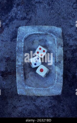 Kleine Marmorschale mit drei Vintage-Würfeln mit roten und blauen Markierungen, die 1 und 3 und 4 zeigen Stockfoto