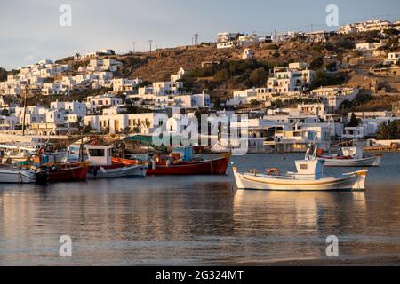 Griechische Fischerboote im Hafen der Insel Mykonos, weiß getünchte Gebäude, Stadtbild im Hintergrund. Kykladen, Griechenland. Bunte traditionelle Boote auf Ruhe verankert Stockfoto