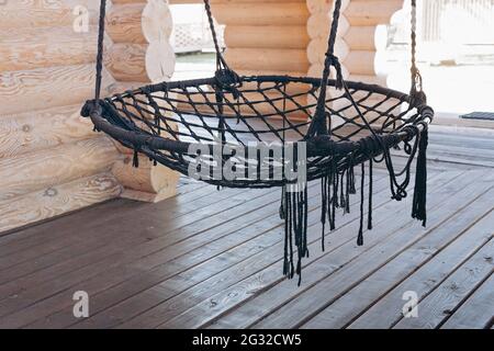 Hängender runder Hängesessel zum Entspannen auf der offenen Terrasse eines Holzhauses. Erholung auf dem Land und Entspannung in der Natur im Sommer. Speicherplatz kopieren. Stockfoto