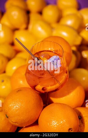 Sommerliche Erfrischung Aperitif-Cocktail in Weinglas mit Eisfelsen, Bambusstroh und geschnittenen Orangen in frischen Orangen und Limetten Hintergrund Stockfoto