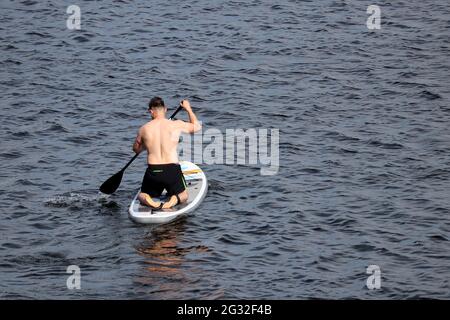 SUP-Surfen, muskulöser Mann mit Paddel, der auf einem Brett im Wasser kniet. Stand-up-Paddleboarding, Sommerurlaub Stockfoto