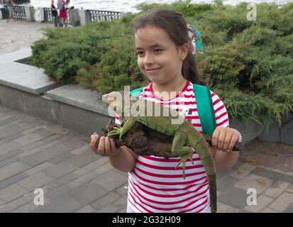 Dnepropetrovsk, Ukraine - 06.12.2021: Ein junges Mädchen hält einen grünen Leguan in den Armen. Emotionen eines Kindes beim Anblick eines Reptils. Stockfoto