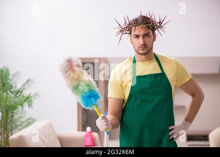 Junger männlicher Auftragnehmer, der auf dem Kopf einen stacheligen Kranz trägt und Hausarbeit leistet Stockfoto