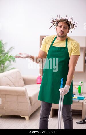 Junger männlicher Auftragnehmer, der auf dem Kopf einen stacheligen Kranz trägt und Hausarbeit leistet Stockfoto