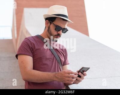 Mann, der sein Smartphone benutzt, während er einen Hut und eine Brille trägt. Stockfoto
