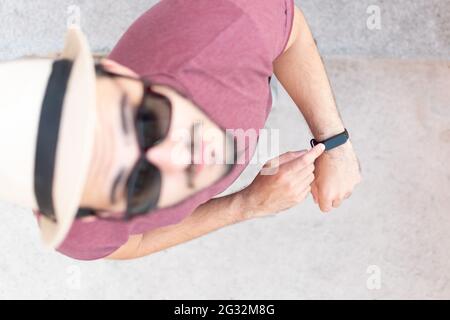 Draufsicht auf einen jungen Mann, der seine smarte Uhr trägt, während er nach oben schaut. Stockfoto