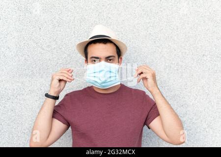 Junger Mann mit Hut, der blaue Maske aufsetzt Stockfoto