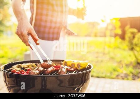 Mann macht Grill, verschiedene Gemüse und Hähnchenflügel mit Würstchen, Grillen auf einem tragbaren Grill im Freien in einem Park in der Natur Stockfoto