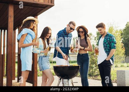 Glückliche Freunde, die Abendessen auf Picknick mit Grill in der Natur, im Freien, junge Menschen essen Grill, Sommer-und Freundschaftskonzept Stockfoto