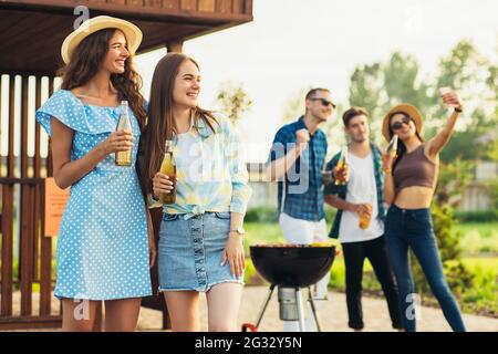 Junge Freunde haben Spaß beim Grillen von Fleisch beim Grillen bereiten SICH EINE Gruppe glücklicher Jungs und Mädchen auf ein Barbecue-Abendessen im Freien vor und essen es Stockfoto