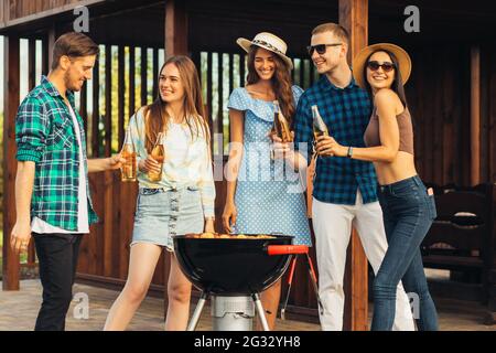 Gruppe von Freunden, die Grill im Hinterhof, Gruppe von glücklichen Freunden Vorbereitung Grill und Mittagessen in der Natur, Picknick im Park auf einem sonnigen s Stockfoto