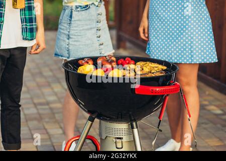 Mann macht Grill, verschiedene Gemüse und Hähnchenflügel mit Würstchen, Grillen auf einem tragbaren Grill im Freien in einem Park in der Natur Stockfoto