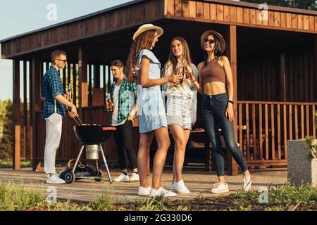 Junge Freunde haben Spaß beim Grillen von Fleisch beim Grillen bereiten SICH EINE Gruppe glücklicher Jungs und Mädchen auf ein Barbecue-Abendessen im Freien vor und essen es Stockfoto