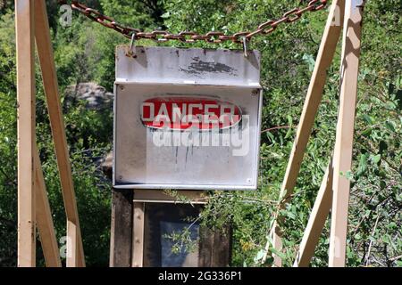 Verwittertes rot-weißes Gefahrenschild mit einer Metallkette oben auf der Treppe, die zu einer alten Pumpstation, Rainbow Pool, Groveland, CA, führt. Stockfoto